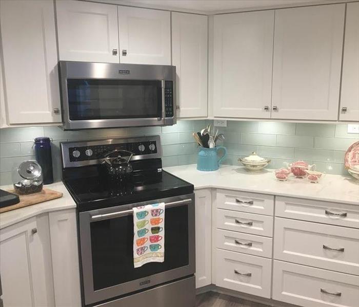 Kitchen with white cabinets, teal backsplash, and black oven