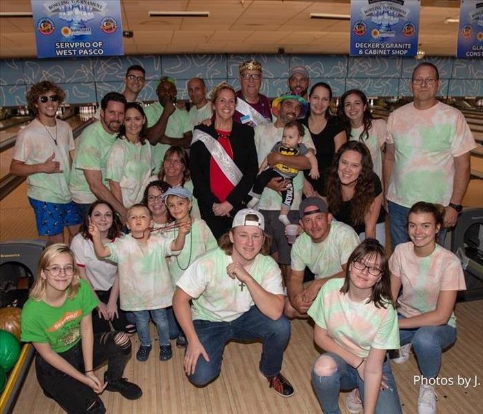 a group of adults standing in front of bowling lanes in tie dye shirts