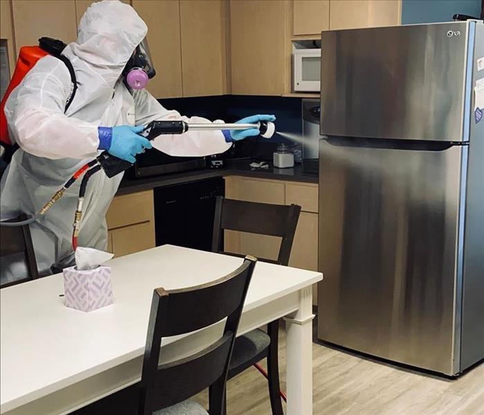 man in tyvek suit disinfecting a fridge